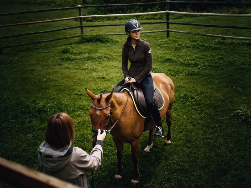Kind mit Reithelm auf einem kleinen Pony im Paddock, vom Erwachsenen am Strick geführt